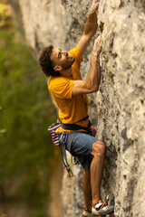 A man in a yellow shirt is climbing a rock wall