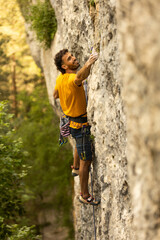 A man in a yellow shirt is climbing a rock wall