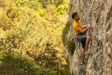 A man in a yellow shirt is climbing a rock wall