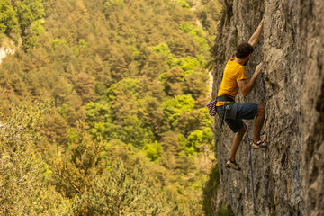 A man in a yellow shirt is climbing a rock wall