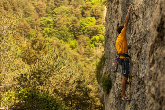 A man is climbing a rock wall wearing a yellow shirt and blue shorts