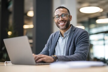 A smiling businessman working on a laptop in a modern office with natural lighting and soft colors, and a minimalistic office background.