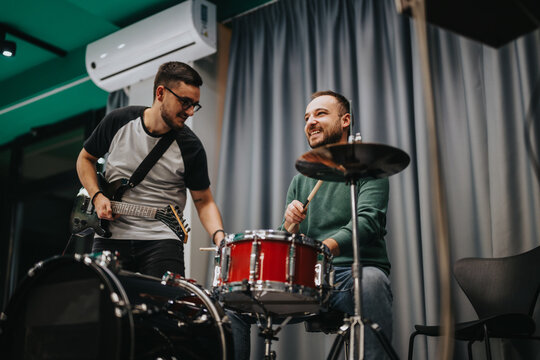Two friends play drums and electric guitar in a fun and creative jam session. They enjoy making music and building on each other's musical energy in an indoor setting.