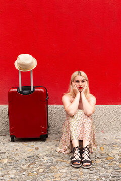 Woman in summer dress travelling with red suitcase in front of a red wall