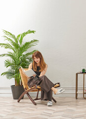 A woman is reading a book at home, looking at the phone and tablet. Decorative interior style and vase of plant.