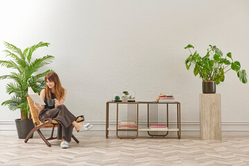 A woman is reading a book at home, looking at the phone and tablet. Decorative interior style and vase of plant.