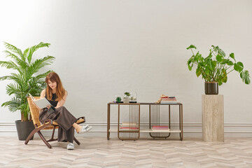 A woman is reading a book at home, looking at the phone and tablet. Decorative interior style and vase of plant.