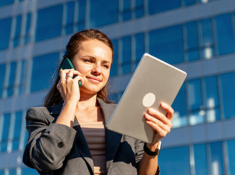 Professional woman using digital tablet during phone call outdoors in city