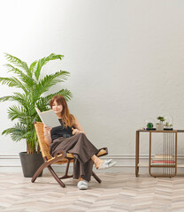 A woman is reading a book at home, looking at the phone and tablet. Decorative interior style and vase of plant.