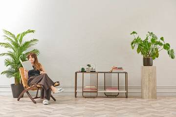 A woman is reading a book at home, looking at the phone and tablet. Decorative interior style and vase of plant.