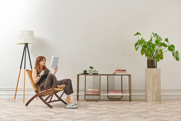 A woman is reading a book at home, looking at the phone and tablet. Decorative interior style and vase of plant.