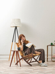 A woman is reading a book at home, looking at the phone and tablet. Decorative interior style and vase of plant.
