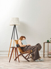 A woman is reading a book at home, looking at the phone and tablet. Decorative interior style and vase of plant.