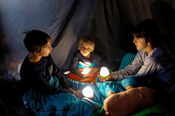 Children, siblings, enjoying a night in a tent in camping, laughing and reading books