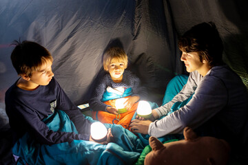 Children, siblings, enjoying a night in a tent in camping, laughing and reading books