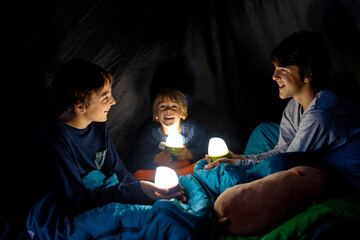 Children, siblings, enjoying a night in a tent in camping, laughing and reading books