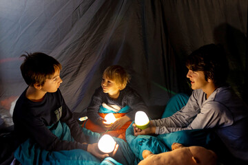 Children, siblings, enjoying a night in a tent in camping, laughing and reading books