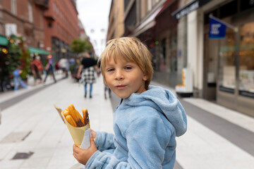 Cute blond child, eating churros on the street in the city of Stockhlom, sweet desert sold on every corner