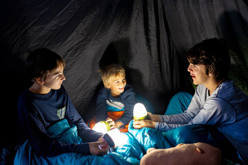 Children, siblings, enjoying a night in a tent in camping, laughing and reading books