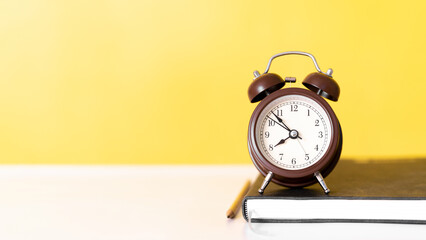 classic alarm clock and yellow pencil on stacked books illustrating time management and education focus, isolated on yellow background