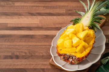 Fresh pineapple chunks served in a pineapple bowl on wooden table background.