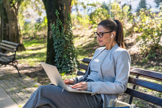 Professional occupation woman sitting on park bench, focused on laptop work blending outdoor relaxation with productivity showcasing modern remote working digital nomad lifestyle and urban tranquility