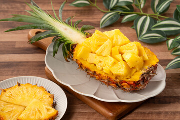 Fresh pineapple chunks served in a pineapple bowl on wooden table background.