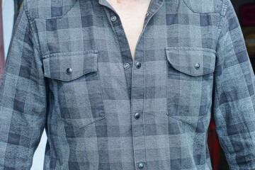 front classic cotton gray black check traditional with round buttons and two pockets stylish with sleeves shirt worn by a man during the day on the street