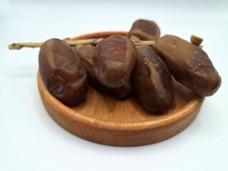Date palm fruit on a small wooden plate. Date palm fruits, or simply dates, are the oval-shaped, sweet, edible fruit of the date palm tree (Phoenix dactylifera)
