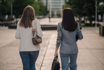 Businesswomen walking away in the city holding bags and laptop