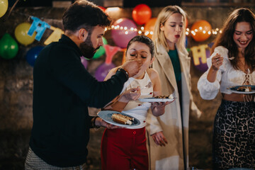 A group of friends sharing food and enjoyment at an outdoor celebration with decorations and warm lighting. Cheerful expressions and a casual setup highlight the joy of the gathering.