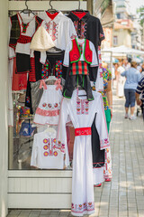 Traditional national Bulgarian folk costumes for kids and adults displayed outside local shop. Concept of cultural heritage, cultural fashion, cultural preservation