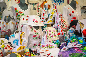 Painted fashion items with vibrant floral designs displayed on market stand in artistic composition. Concept of wearable art, custom design, creative expression
