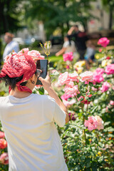 Person with red bandana photographing blooming roses with smartphone during sunny outdoor event. Concept of mobile photography, nature beauty, creative moment, modern technology