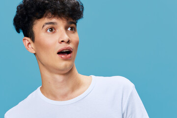 surprised man with curly hair wearing white t-shirt looking amazed on blue background, young adult showing shocked facial expression, casual style portrait
