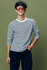 smiling man wearing striped shirt and sunglasses standing against green background, casual style, youthful energy and modern fashion, confident posture