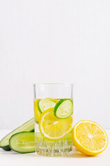 Refreshing homemade detox water infused with fresh green cucumber and sour lemon citrus fruit slices served in one glass on white wooden table with copy space with ingredients as antioxidant drink