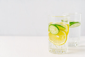 Refreshing organic homemade detox water made with fresh juicy cucumber slices and sour lemon citrus fruit served in glass on white wooden table with copy space as healthy antioxidant summer drink