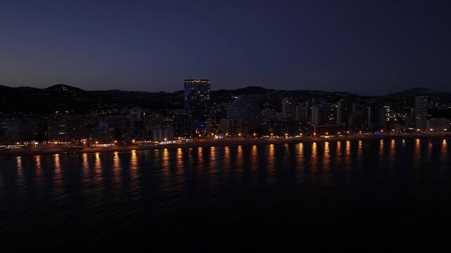 Calp city waterfront with illuminated buildings and Estimar hotel reflecting at night, Spain.