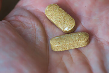 Male hand holds two tablets with vitamins, to increase immunity. Dietary supplements. Selective focus