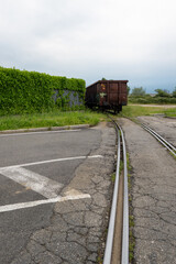 Rusty freight wagon on narrow rails disappearing into overgrown industrial area with cracked asphalt