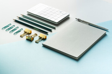 Office supply, notebook, calculator, pencils and binder clips flat lay on blue background.