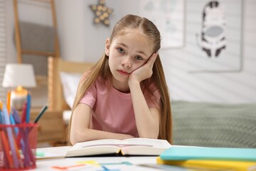 Dyslexia. Upset little girl reading book at table indoors