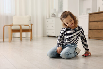 Little girl playing with toy car on floor at home, space for text