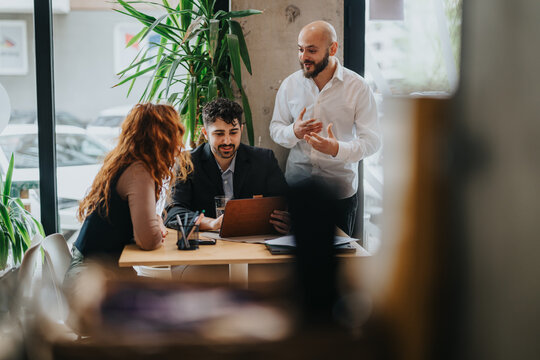 A team of people collaborates at a stylish co working cafe, engaging in meaningful discussions and brainstorming, with an inviting ambiance enhanced by natural light and vibrant greenery. - Powered by Adobe
