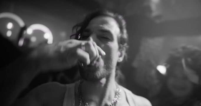 Man Enjoys Alcohol Shots and Dances Energetically at a Stylish Party, Surrounded by a Lively Crowd and Pulsating Lights, Capturing the Essence of Nightlife and Celebration. Black and White Footage