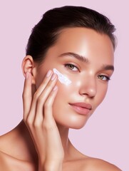 Close-up of young woman with healthy radiant skin and skincare cream, pink background.
