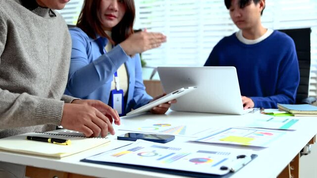 Professionals analyzing data and reports in office setting with tablet, calculator, and paperwork.