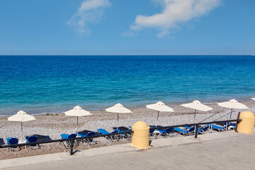 Pristine beach landscape with a vibrant blue sea, white umbrellas and blue sunbeds, offering a sense of calm and escape for travelers.