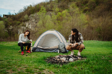 Fototapeta premium Two female friends setting up camp in the forest after hiking or trekking 